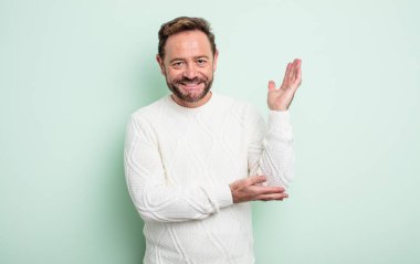 Orta yaşlı yakışıklı adam gururla ve kendinden emin bir şekilde gülümsüyor, mutlu ve tatmin olmuş hissediyor ve fotokopi alanında bir konsept gösteriyor.