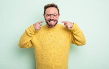 Orta yaşlı, yakışıklı bir adam, kendine güvenerek gülümsüyor. Geniş bir gülümseme, pozitif, rahat, tatmin olmuş bir tavır.