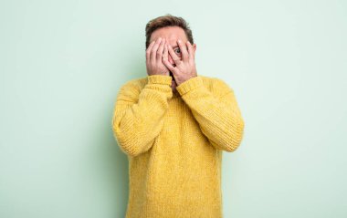 Orta yaşlı yakışıklı bir adam korkmuş ya da utanmış hissediyor. Gözleri yarı kapalı ya da elleri yarı kapalı bir şekilde dikizliyor.