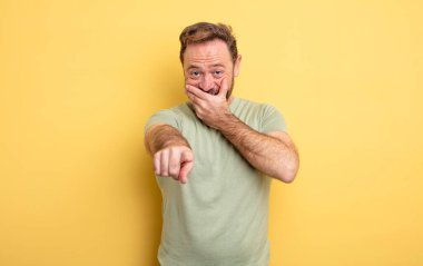 Orta yaşlı yakışıklı adam sana gülüyor, kamerayı gösteriyor ve seninle dalga geçiyor ya da alay ediyor.