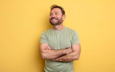 Orta yaşlı yakışıklı adam mutlu, gururlu ve umutlu merak ediyor ya da düşünüyor, çapraz kollarla fotokopi çekmeyi bekliyor.