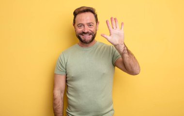 Orta yaşlı yakışıklı bir adam gülümsüyor ve arkadaş canlısı görünüyor. 5 ya da 5 numarayı gösteriyor. Eli önde, geriye doğru sayıyor.