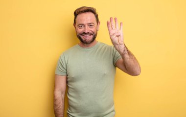 Orta yaşlı yakışıklı adam gülümsüyor ve arkadaş canlısı görünüyor. Elleri önde, geriye doğru sayıyor.