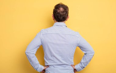 Orta yaşlı yakışıklı bir adam kafası karışık ya da dolu ya da şüphe ve soru dolu, merak ediyor, elleri kalçasında, dikiz aynasından