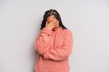 Siyah afro kadın stresli, utanmış ya da üzgün görünüyor, baş ağrısı var, yüzünü eliyle kapatıyor.