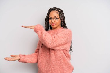 Siyah afro kadın bir objeyi iki eliyle fotokopi alanında tutuyor, bir objeyi gösteriyor, sunuyor ya da reklamını yapıyor.