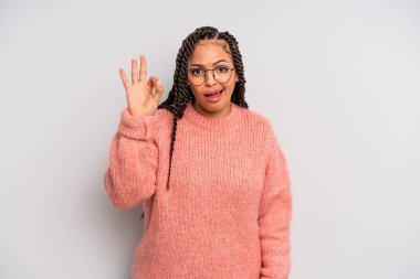 Siyah afro kadın kendini başarılı ve tatmin olmuş hissediyor, ağzı açık gülümsüyor, elle işaret veriyor.