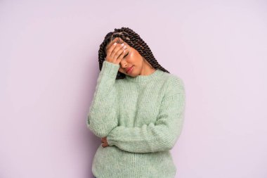 Siyah afro kadın stresli, utanmış ya da üzgün görünüyor, baş ağrısı var, yüzünü eliyle kapatıyor.