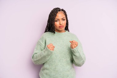 Siyah afro kadın kendinden emin, sinirli, güçlü ve agresif görünüyor. Yumrukları boks pozisyonunda dövüşmeye hazır.