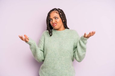 black afro woman shrugging with a dumb, crazy, confused, puzzled expression, feeling annoyed and clueless