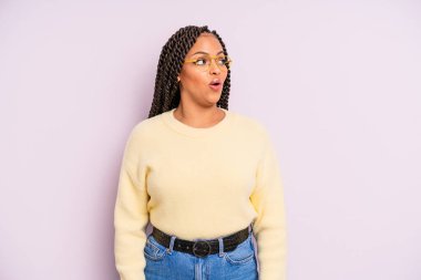 Siyah afro kadın şaşkın, mutlu, şaşkın ve şaşırmış hissediyor, ağzı açık bir şekilde yana bakıyor.