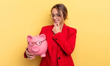 businesswoman smiling with a happy, confident expression with hand on chin. piggy bank concept
