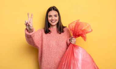pretty woman smiling and looking happy, gesturing victory or peace. trash bag concept