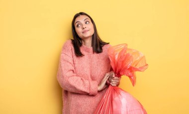 pretty woman shrugging, feeling confused and uncertain. trash bag concept