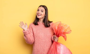 pretty woman smiling happily, waving hand, welcoming and greeting you. trash bag concept
