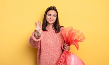 pretty woman smiling and looking friendly, showing number three. trash bag concept