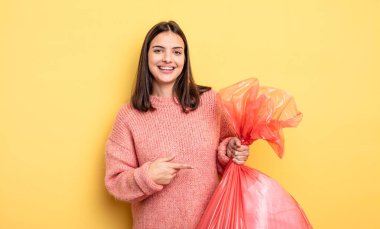 pretty woman smiling cheerfully, feeling happy and pointing to the side. trash bag concept