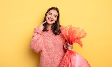 pretty woman smiling confidently pointing to own broad smile. trash bag concept