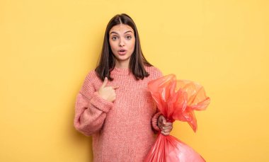 pretty woman looking shocked and surprised with mouth wide open, pointing to self. trash bag concept