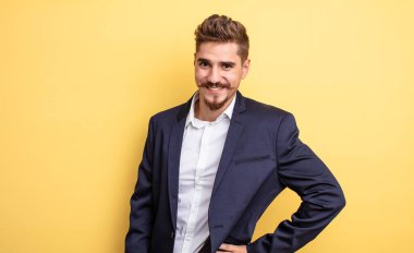 İş adamı mutlu bir şekilde gülümsüyor, eli kalçasında ve kendinden emin.