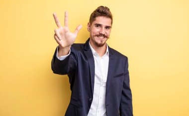 İş adamı gülümsüyor ve arkadaş canlısı görünüyor, üç numarayı gösteriyor.