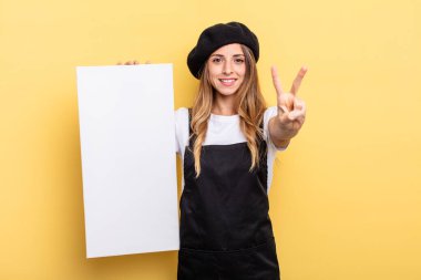 woman artist smiling and looking friendly, showing number two empty canvas concept