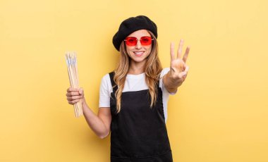 Ressam gülümsüyor ve arkadaş canlısı görünüyor, üç numarayı gösteriyor.