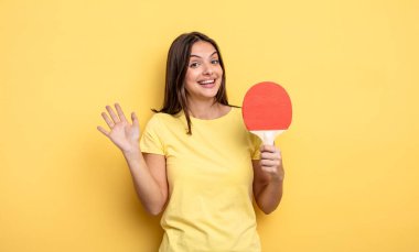 pretty woman smiling happily, waving hand, welcoming and greeting you. ping pong concept