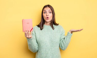 Güzel kadın şaşırmış ve şok olmuş görünüyor. Çenesi düşmüş ve elinde bir nesne tutuyor. planlayıcı konsepti