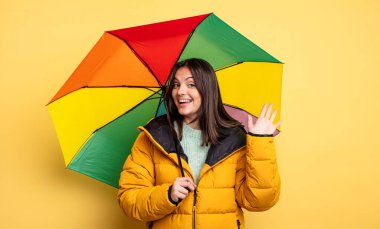 pretty woman smiling happily, waving hand, welcoming and greeting you. winter and umbrella concept