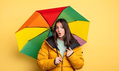 pretty woman looking shocked and surprised with mouth wide open, pointing to self. winter and umbrella concept