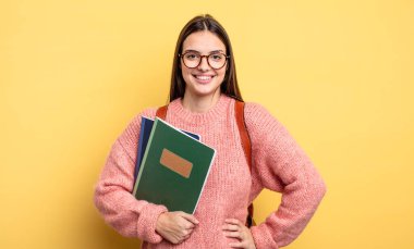 pretty student woman smiling happily with a hand on hip and confident