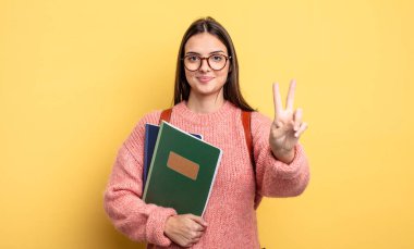 pretty student woman smiling and looking happy, gesturing victory or peace