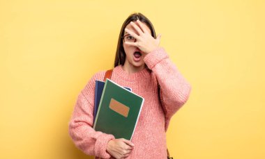 pretty student woman looking shocked, scared or terrified, covering face with hand