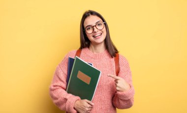pretty student woman smiling cheerfully, feeling happy and pointing to the side