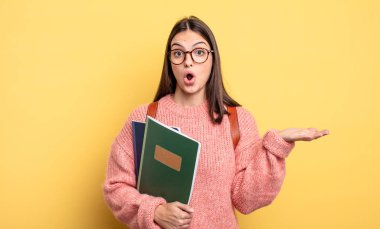 pretty student woman looking surprised and shocked, with jaw dropped holding an object