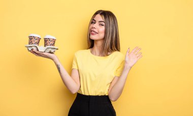 Güzel bir kadın mutlu bir şekilde gülümsüyor, el sallıyor, hoş karşılıyor ve seni selamlıyor. kahve konseptini kaldır.