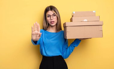 pretty woman looking serious showing open palm making stop gesture packages boxes concept