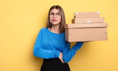 pretty woman shrugging, feeling confused and uncertain packages boxes concept