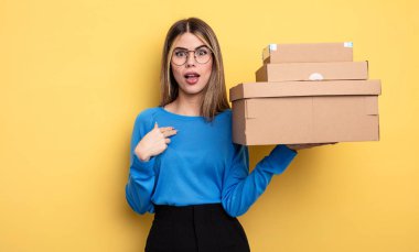 Güzel bir kadın ağzı açık bir şekilde şok olmuş ve şaşırmış görünüyor. Kişisel paket kutuları kavramına işaret ediyor.