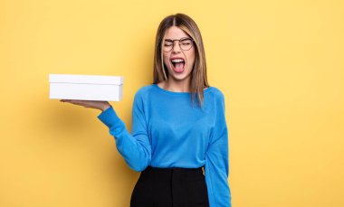 Güzel bir kadın agresif bir şekilde bağırıyor, çok kızgın görünüyor. Beyaz kutu tutuluyor