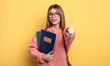 Güzel öğrenci kadın seni seçen kamerayı işaret ediyor. kitaplar ve sırt çantası