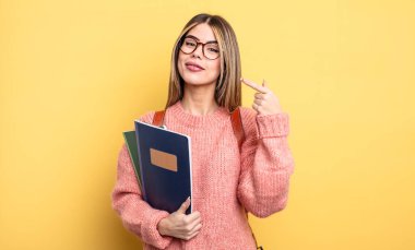 Güzel bayan öğrenci, kendine güvenerek gülümsüyor ve kendi gülüşünü gösteriyor. kitaplar ve sırt çantası