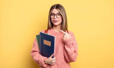 Güzel bayan öğrenci neşeyle gülümsüyor, mutlu hissediyor ve bir tarafı işaret ediyor. kitaplar ve sırt çantası