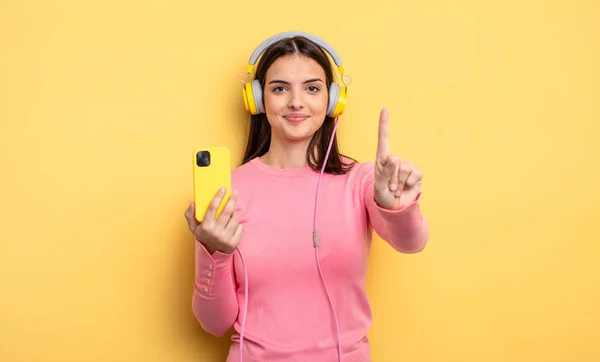 Pretty Woman Smiling Looking Friendly Showing Number One Listening Music — Stockfoto