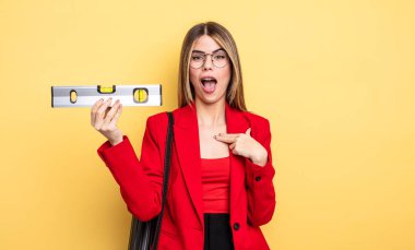 Mimar kadın şaşkın ve şaşırmış görünüyor ağzı açık, kendini işaret ediyor ve dengeyi koruyor.