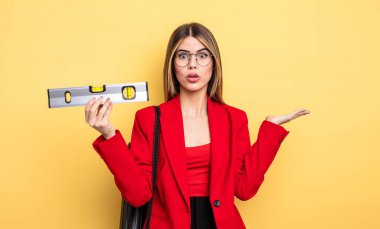 Mimar kadın şaşırmış ve şok olmuş görünüyor, çenesi düşmüş bir nesneyi tutuyor ve dengeyi koruyor