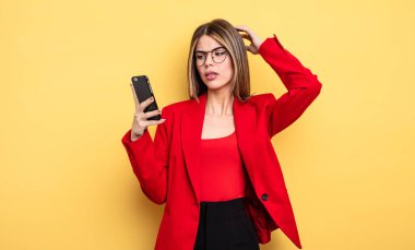 İş kadını şaşkın ve kafası karışık, kaşınan bir kafa hissediyor. akıllı telefon kavramı