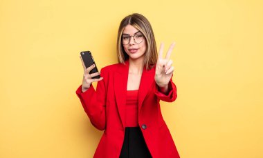 Gülümseyen ve mutlu görünen iş kadını, zafer ya da barış işareti yapıyor. akıllı telefon kavramı