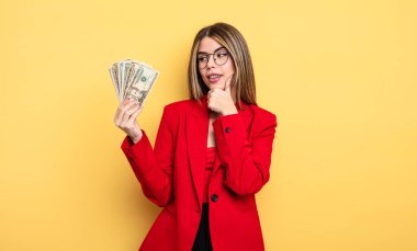 İş kadını mutlu ve kendinden emin bir ifadeyle gülümsüyor, elleri çenesinde. Dolar banknotları konsepti